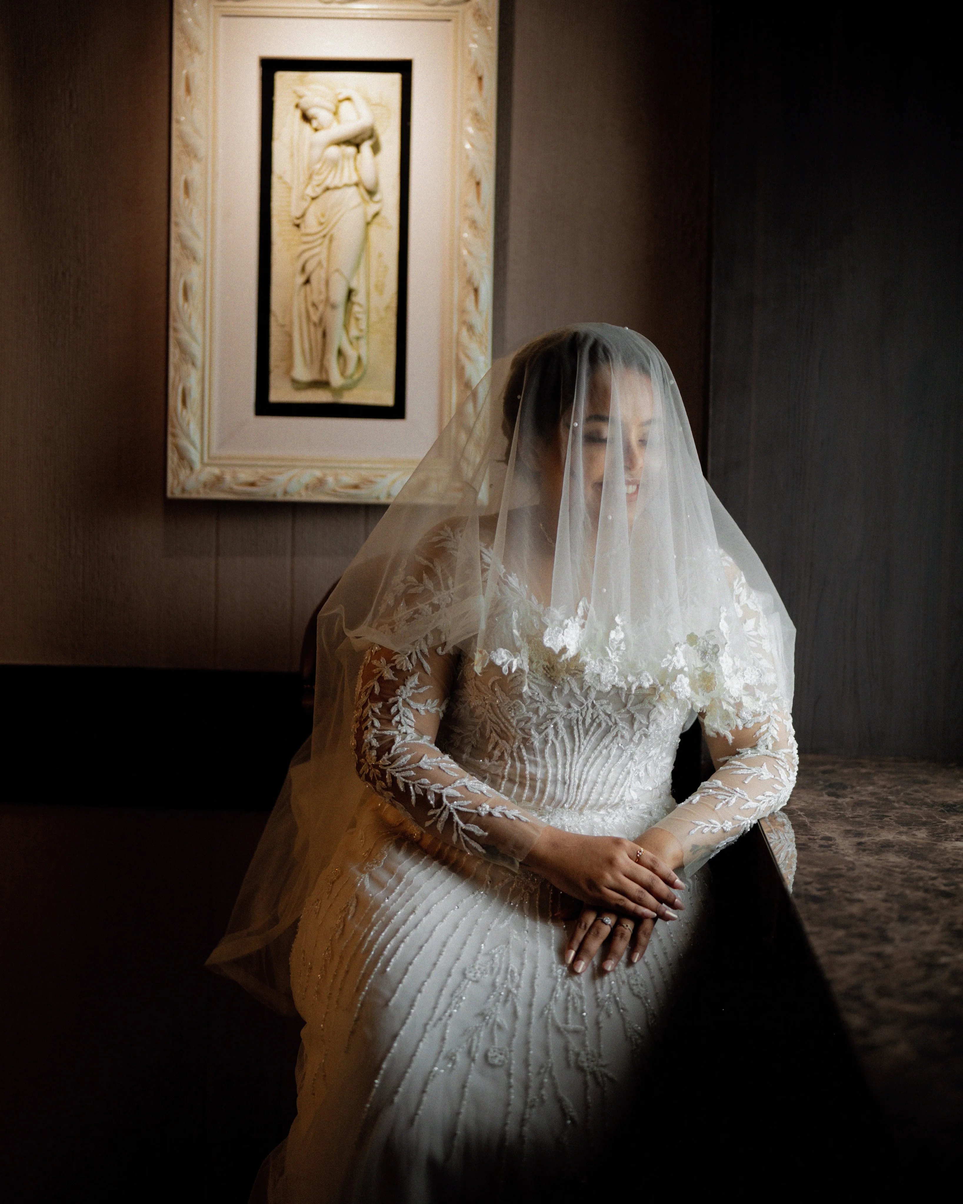A bride seated in soft window light beneath her veil